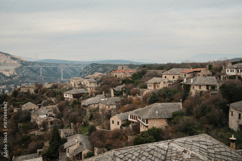 Obraz premium Traditional stone houses of Pocitelj village spread across a steep hillside with historic architecture and rugged terrain in Bosnia and Herzegovina.