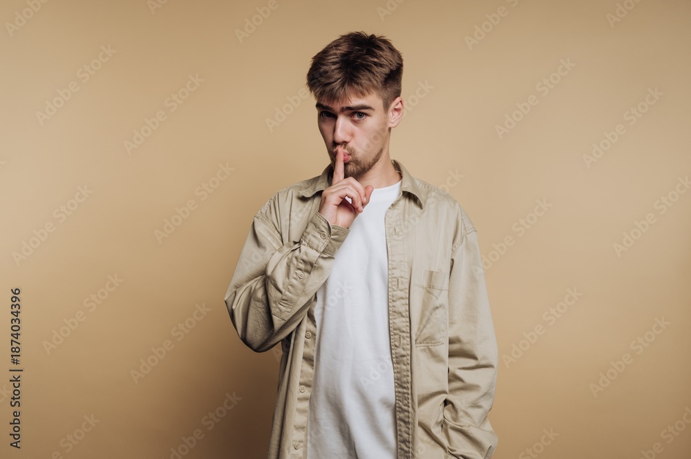 Fototapeta premium Young man making a shushing gesture with his finger on his lips in front of a plain background