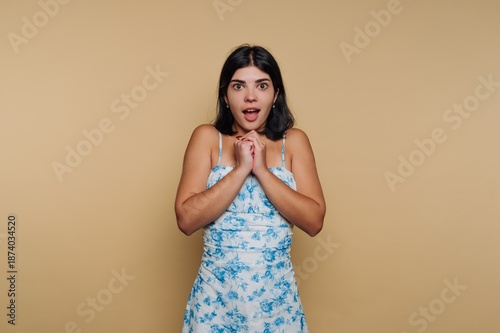 Fotografie Surprised young woman shows excitement with hands clasped together in studio set