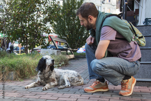 Cuadro en lienzo Adult man crouching on a city sidewalk watching a homeless dog resting on the pa