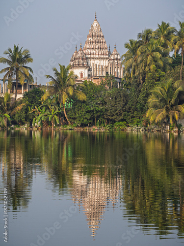 Vertical landscape view of ancient Bhubaneshwar Shiva temple and trees with reflection in lake, Puthia, Rajshahi, Bangladesh