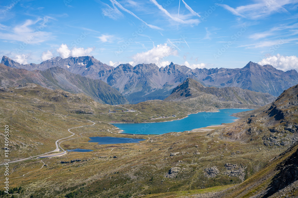 Fototapeta premium Lago Bianco reservoir stands majestically at Bernina Pass in Switzerland. Surrounded by towering alpine mountains, the tranquil lake reflects the stunning landscape under a clear sky.