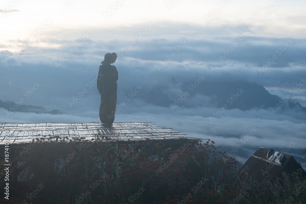 Fototapeta premium Silhouette of a traveler standing quietly on a wooden platform at sunrise