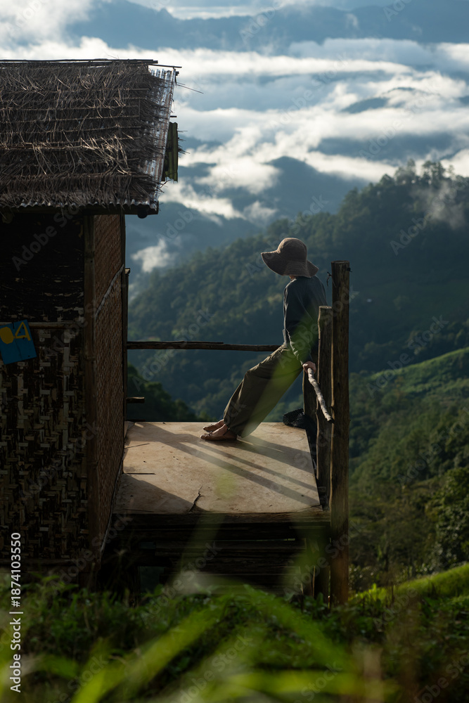 Fototapeta premium Silhouette of a person resting on a wooden balcony overlooking misty mountains