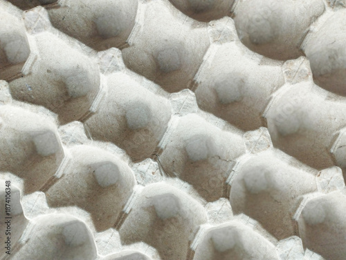 A top-down, close-up view of an empty grey molded pulp egg tray, showing a repetitive geometric pattern and textured paper surface.