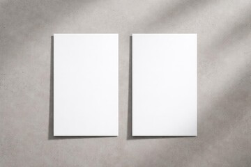 Birds eye flat lay of two blank white vertical rectangle menu mockups featuring gentle shadows on a neutral light grey concrete surface
