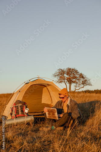 Traveling male freelancer typing on laptop while sitting near camping tent during remote work in nature  