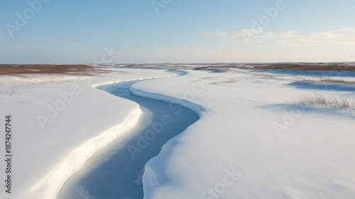 A frozen river winds through a vast, snow-covered landscape under a clear blue sky.