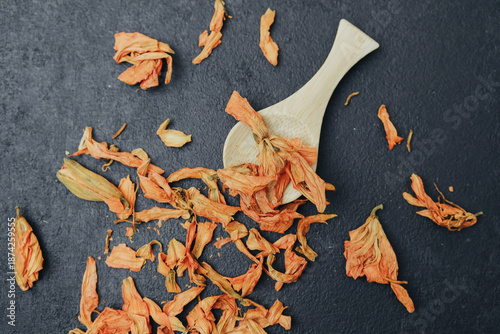 Fotografi Dried orange flower petals scattered on dark surface with wooden scoop