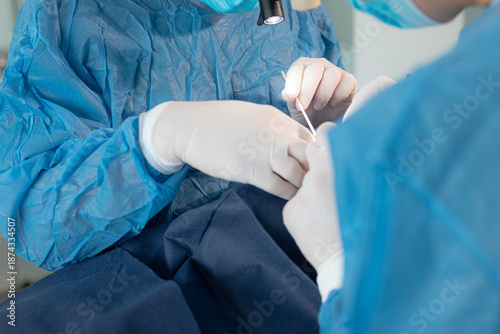 Medical team performing a blepharoplasty procedure, using an electrocautery pen tool to coagulate blood vessels and stop bleeding on a patient's eyelid in a sterile operating room.