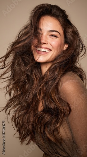 Happy woman with beautiful long wavy brown hair laughing and smiling while posing in a studio, expressing joy, natural beauty, and positive emotion