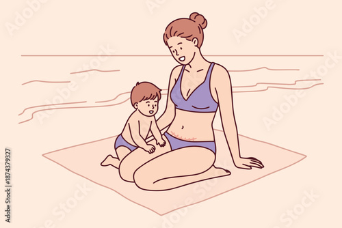 Happy woman with visible cesarean section scar sits on beach towel with her small son. Mother enjoys summer vacation and childhood moments, embracing her body after childbirth and surgery.