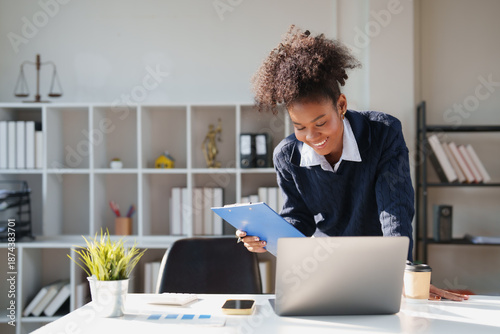 Foto Smiling young black woman reviewing documents while working with a laptop in a b