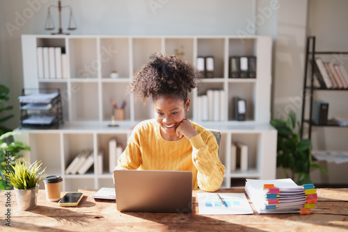 Fotografie Young African American woman in a yellow sweater smiling as she types on a lapto