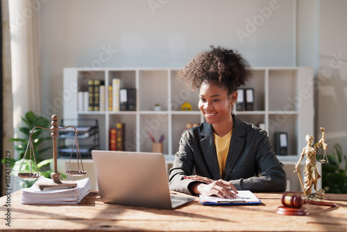 Fotografie Young African American woman lawyer smiling at laptop while preparing legal docu