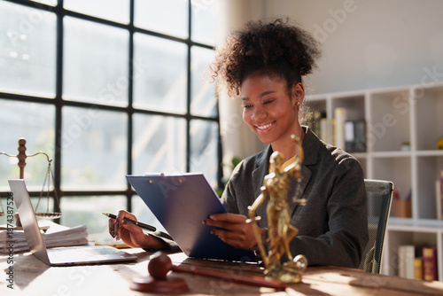 Foto Young African American female lawyer sitting at her desk, reviewing and writing