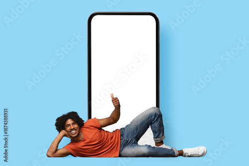 Εκτύπωση καμβά Cheerful handsome young black guy in casual chilling by huge smartphone with whi