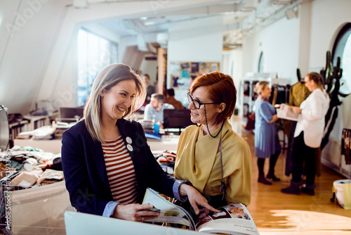 Adult coworkers smiling while reviewing fashion catalog in creative studio