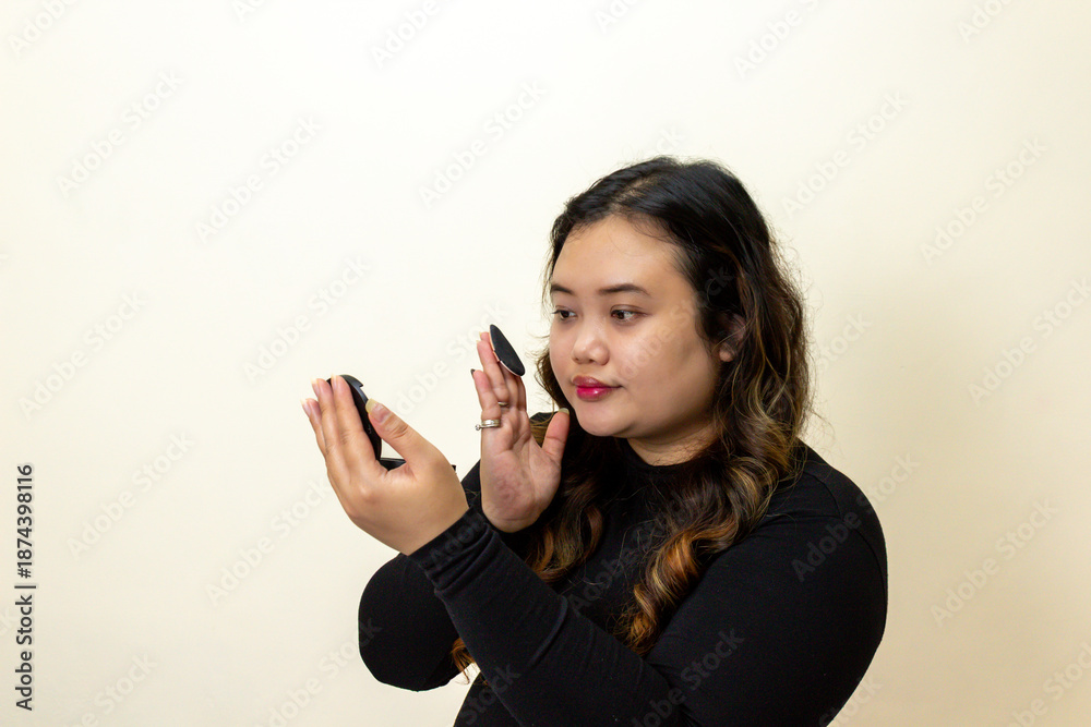 Fototapeta premium Young Woman Applying Makeup Using Compact Mirror and Powder Puff