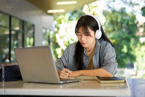 Cuadro en lienzo asian woman college student wearing headphone looking at laptop sitting at table