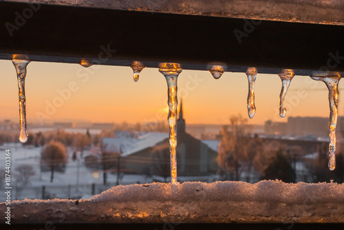 Winter dawn. Icicle in the rays of the morning sun. Cityscape. Cold weather. Frosty morning. Hard water. Ice patterns. Beauty of nature. Reflections in the ice. Frozen moment. Melting ice. Icy roof. 