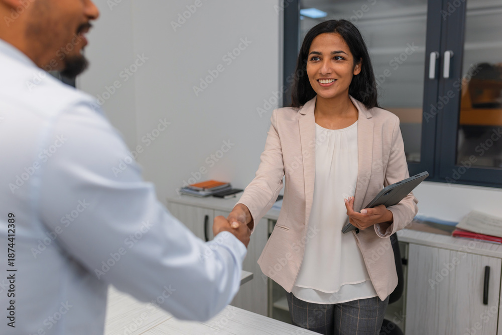 Fototapeta premium Professionals meet and shake hands in an office. They discuss hiring, onboarding, and future work opportunities.