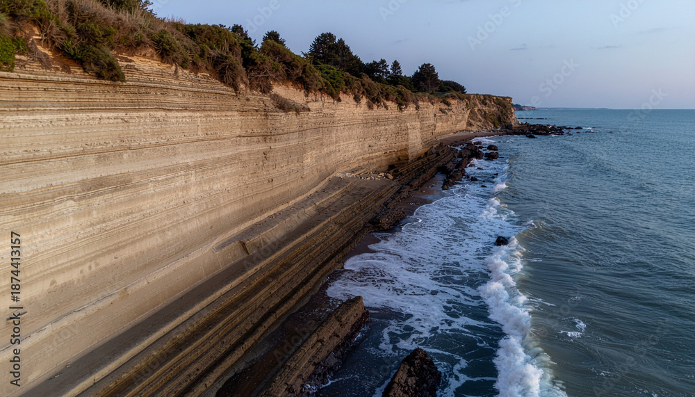 Obraz premium A serene ocean view with waves crashing against a layered cliffside at dusk