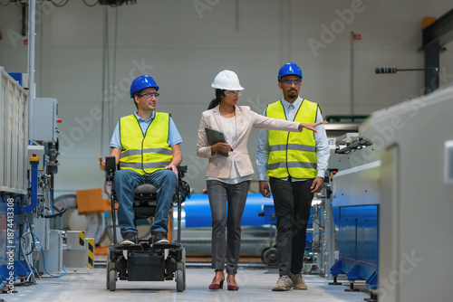 Foto A female manager guides male factory workers and a worker with disability in a wheelchair through production operations in a manufacturing plant