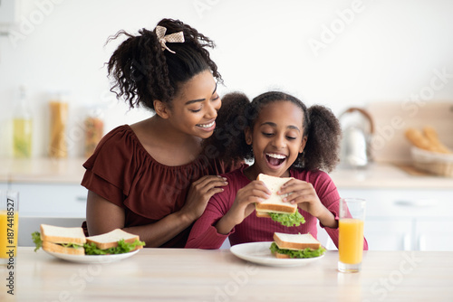 Cuadro en lienzo Loving black mother and daughter cuddling while having snack at kitchen, eating