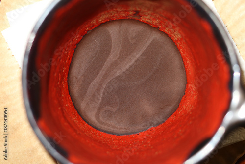 Red and black ceramic coffee cup with coffee grounds.
