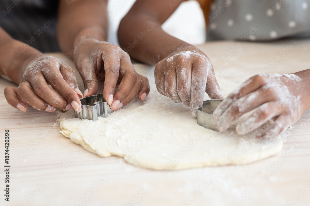 Fototapeta premium Closeup of afro-american family mother and daughter hands making diverse figures with cookie cutters, black mom and kid baking together at home, using biscuit figurines, baking concept