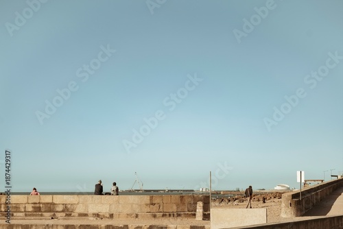 Fotografie Visitors relax on a scenic stone promenade in Porto, soaking in the warm sun and gentle ocean breeze