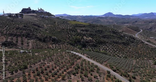 Aerial drone shot panorama wide view of the white town village of Olvera in Andalusia, Spain, Europe. Traditional castle and church on hill, and olive trees. Drone orbiting
