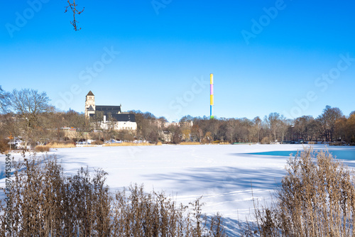 Frozen Schlossteich lake in public park with city landmarks in winter, Chemnitz Germany, snow covered ice, clear blue sky and calm urban park scenery