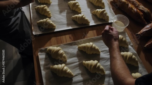 A baker brushes croissants with egg yolks before baking. Traditional process for making French croissants in an artisan bakery.