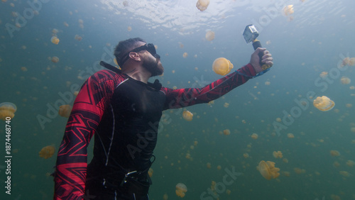 Underwater shot of the freediver swimming in the lake full of jellyfish with action camera