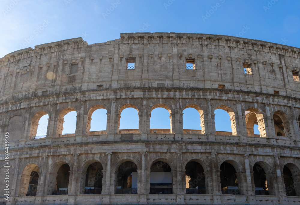 Obraz premium Famous Coliseum in Rome. Colosseum, or Coliseum. Part of the wall of an antique stone structure with arches. Italy, Europe. Famous touristic place in the world, Europe. Beautiful blue sky background.