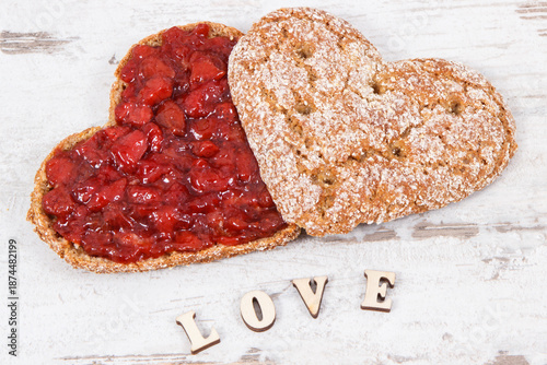 Fresh baked bread in shape of heart with strawberry jam and inscription love. Rustic background