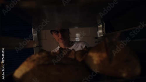 Baker loading freshly baked artisan bread onto industrial metal racks and moving around bakery space. Transferring hot loaves for cooling in a professional bakery production process. Freshly baked.