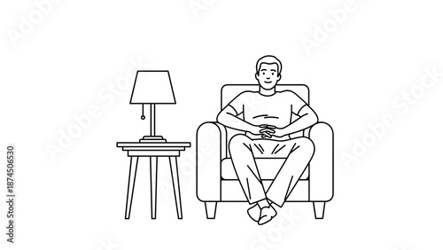 A young man relaxes comfortably in a plush armchair next to a side table with a lit lamp, his hands clasped in his lap, signifying leisure, downtime, and peaceful enjoyment of his home environment.