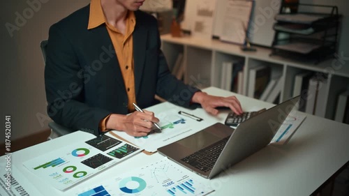 Focused businessman working late at night, analyzing financial charts and graphs. Professional using a laptop and calculator for business analysis