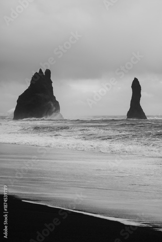 Dramatic black and white vertical photograph of the Reynisdrangar sea stacks at Reynisfjara black sand beach, Iceland.