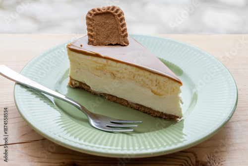 Fotografia A decadent slice of creamy cheesecake topped with caramel and a biscuit, presented on a ridged green plate with a fork