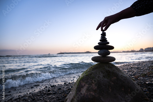 A girl's hand stacks stones into a pyramid on the beach