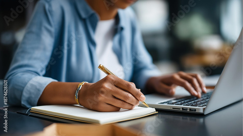 Faceless young business woman sitting at desk scrolling laptop taking notes notebook  closeup hand writing pen professional productivity workplace documentation