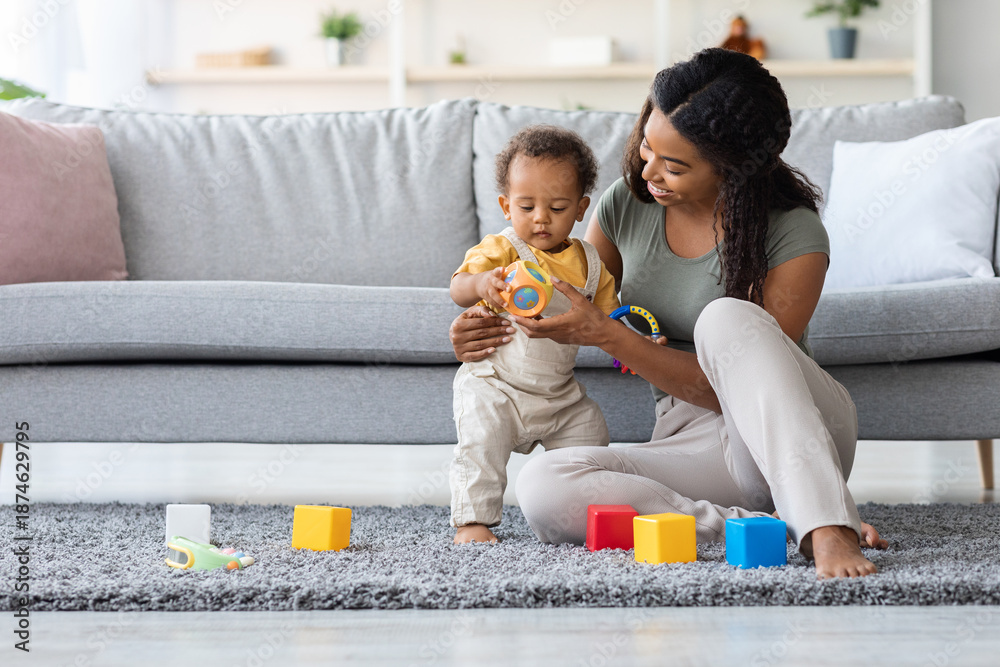Fototapeta premium Caring Black Mom And Her Adorable Infant Son Playing With Toys At Home, Young African American Mother Spending Time With Cute Toddler Child, Having Fun Together In Living Room, Copy Space