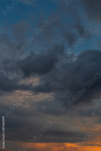 A moody, cloud-filled sky at sunset spills warm orange light across the horiz...