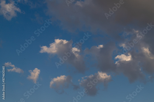 A clear blue sky dotted with fluffy white clouds, bathed in soft sunlight. Pe...