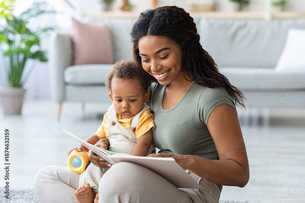 Fototapeta premium Caring African American Mommy Reading Book For Her Adorable Toddler Son At Home, Young Black Woman Bonding With Cute Little Infant Baby, Enjoying Spending Time Together, Closeup Shot With Copy Space