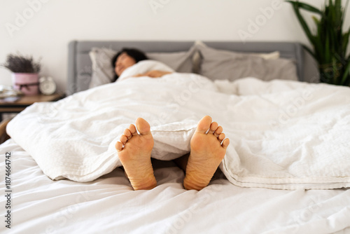 Quadro em tela A person bare feet sticking out from under white bed sheets in a cozy bedroom, r